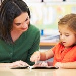 Elementary Pupil Reading With Teacher In Classroom